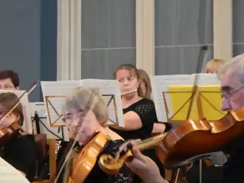 Violinists playing in the foreground while other players watch from behind music stands in a hall